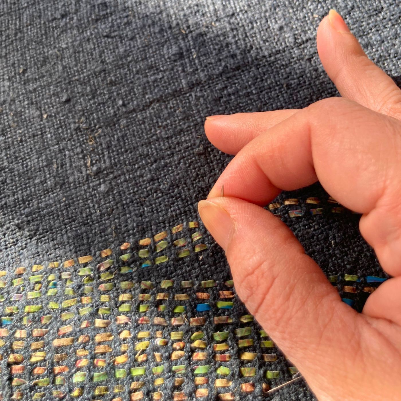 A hand holding a needle stitching into dark a fabric cloth