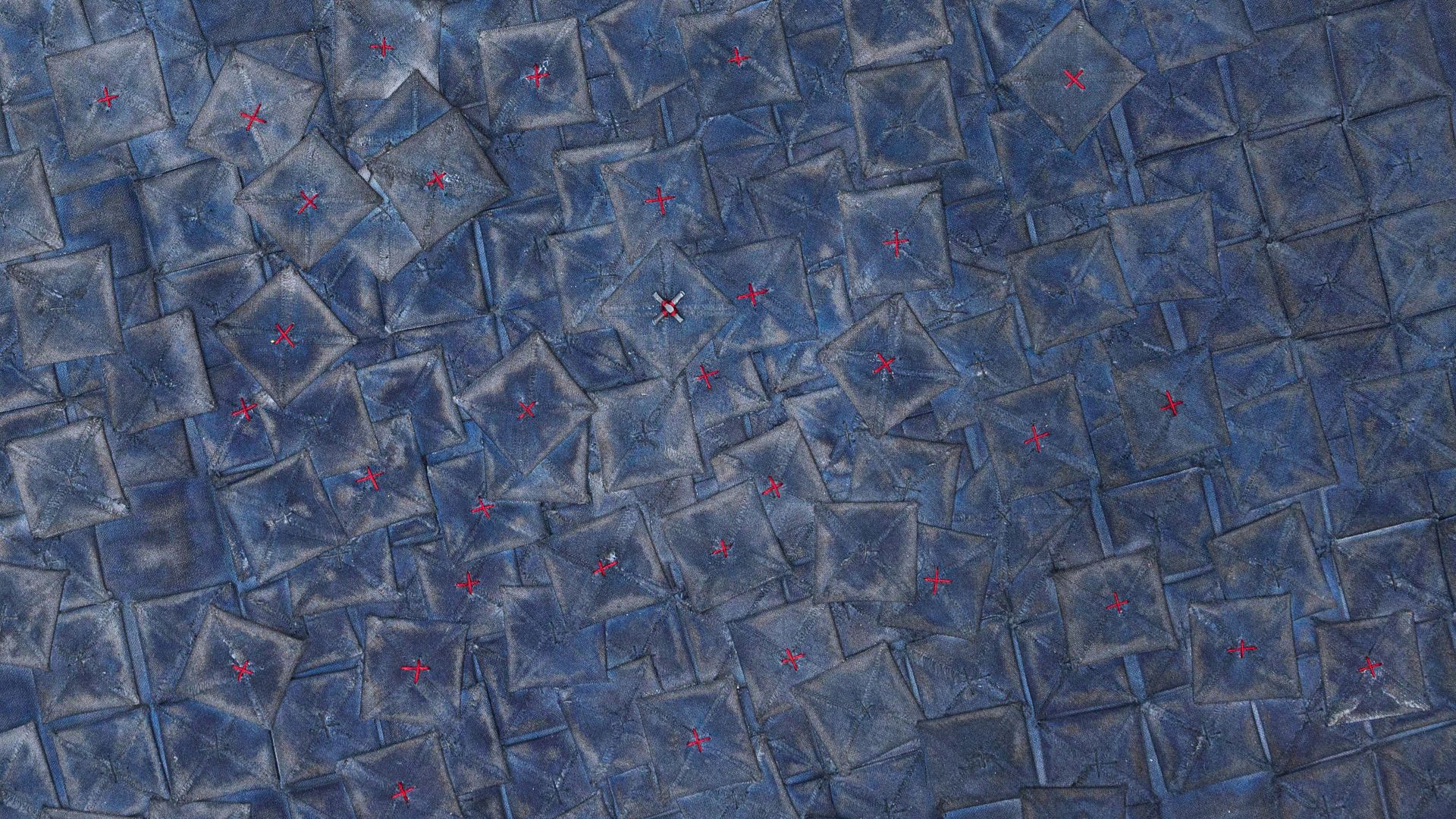 A close up images of a stitched artwork of blue squares with red crosses