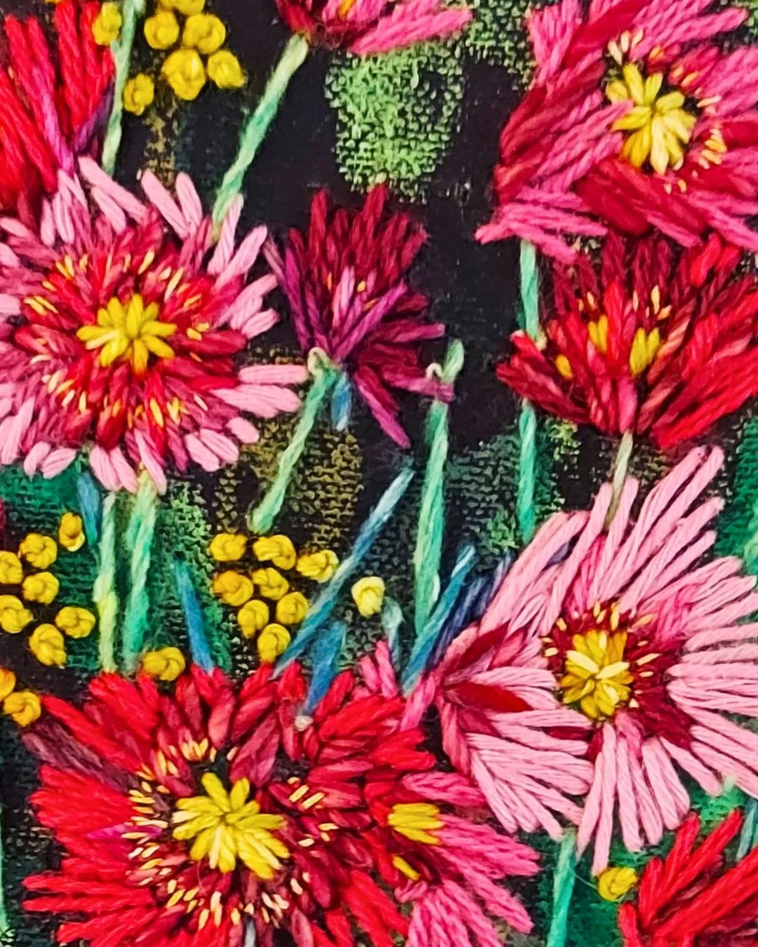 A close-up image of a hand stitched bunch of red and pink flowers on a black background