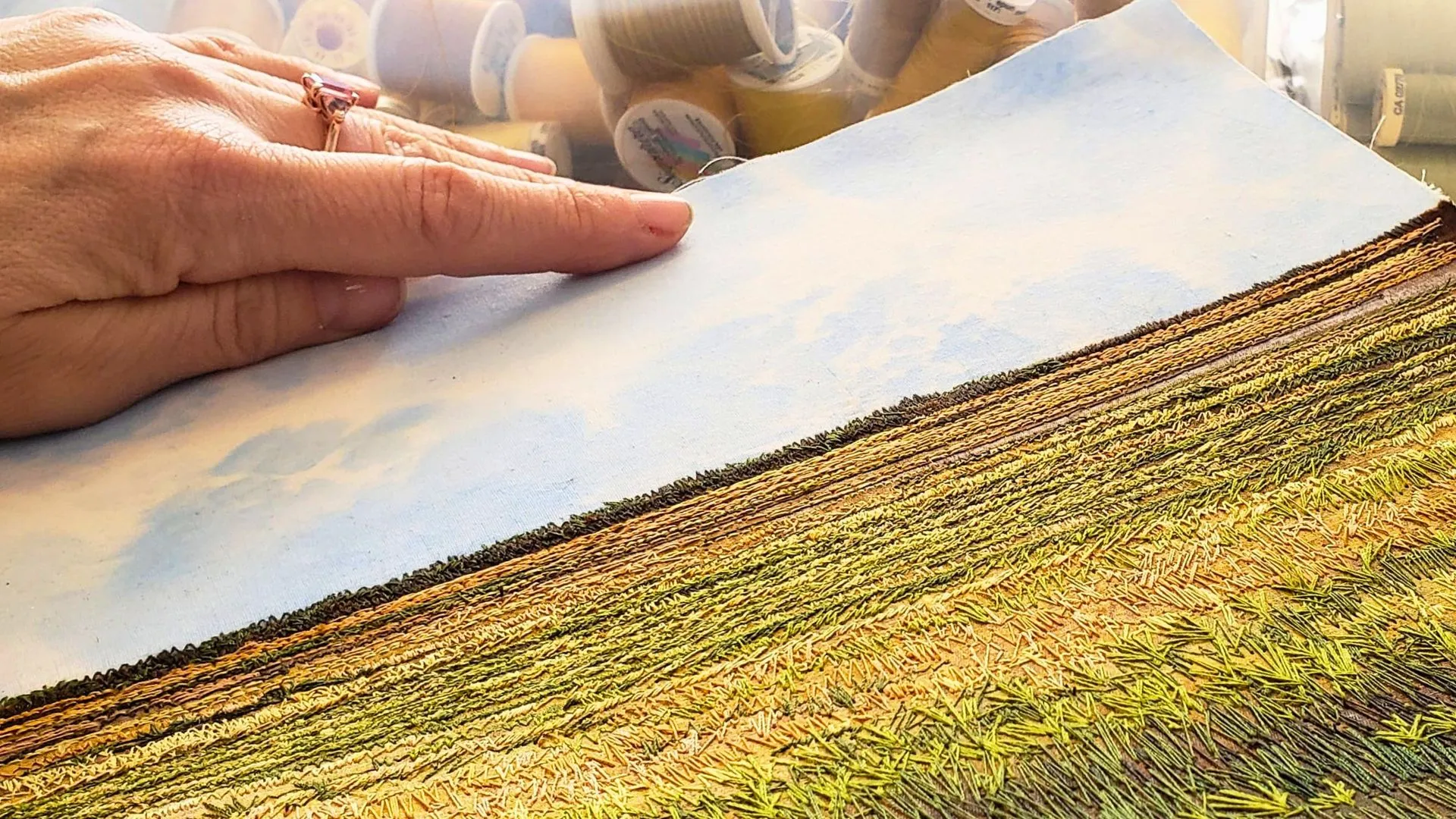 A hand pointing at a stitched landscape 'painting' work in progress