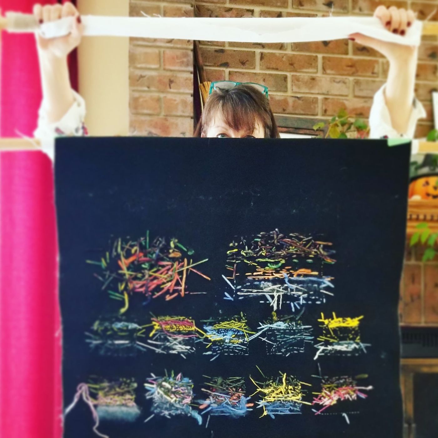 Female artist stood behind a piece of abstract stitched artwork, holding the piece up to show the random stitches on the reverse