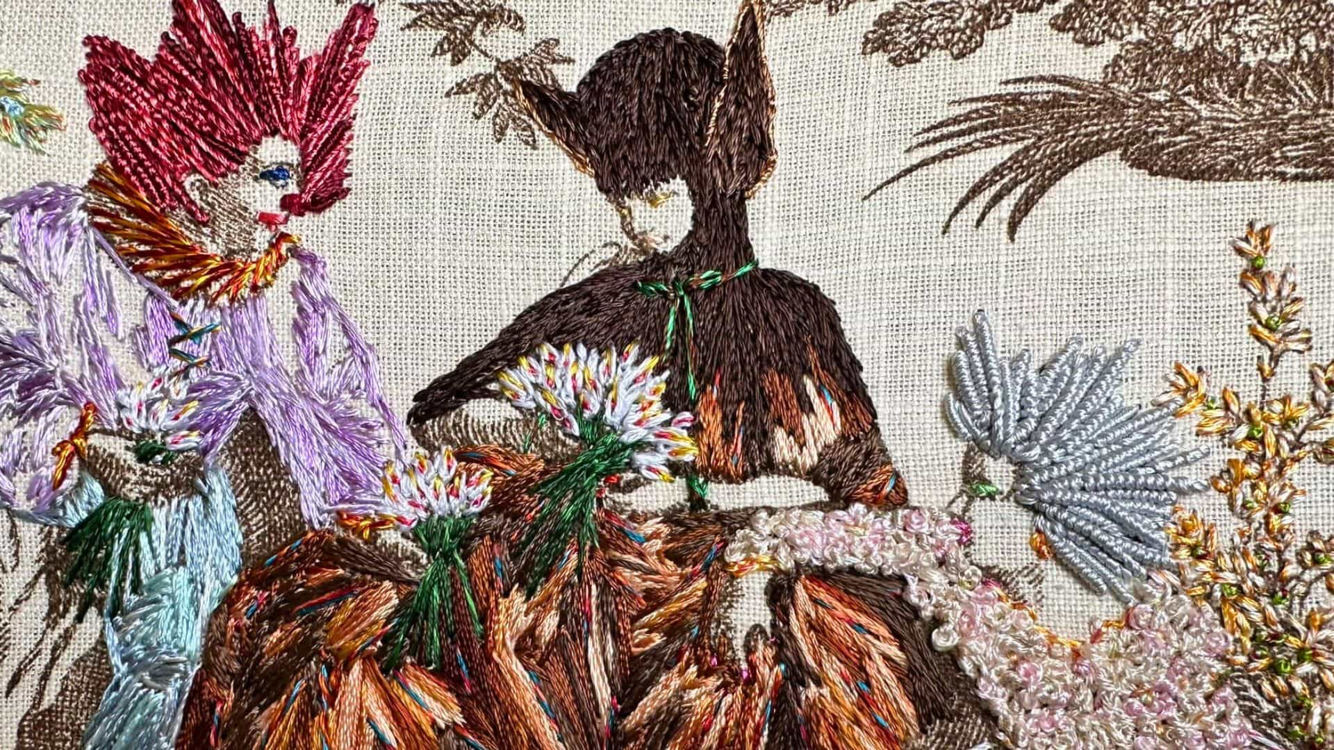 a close up of a fabric with three hand-stitched figures sat conversing.