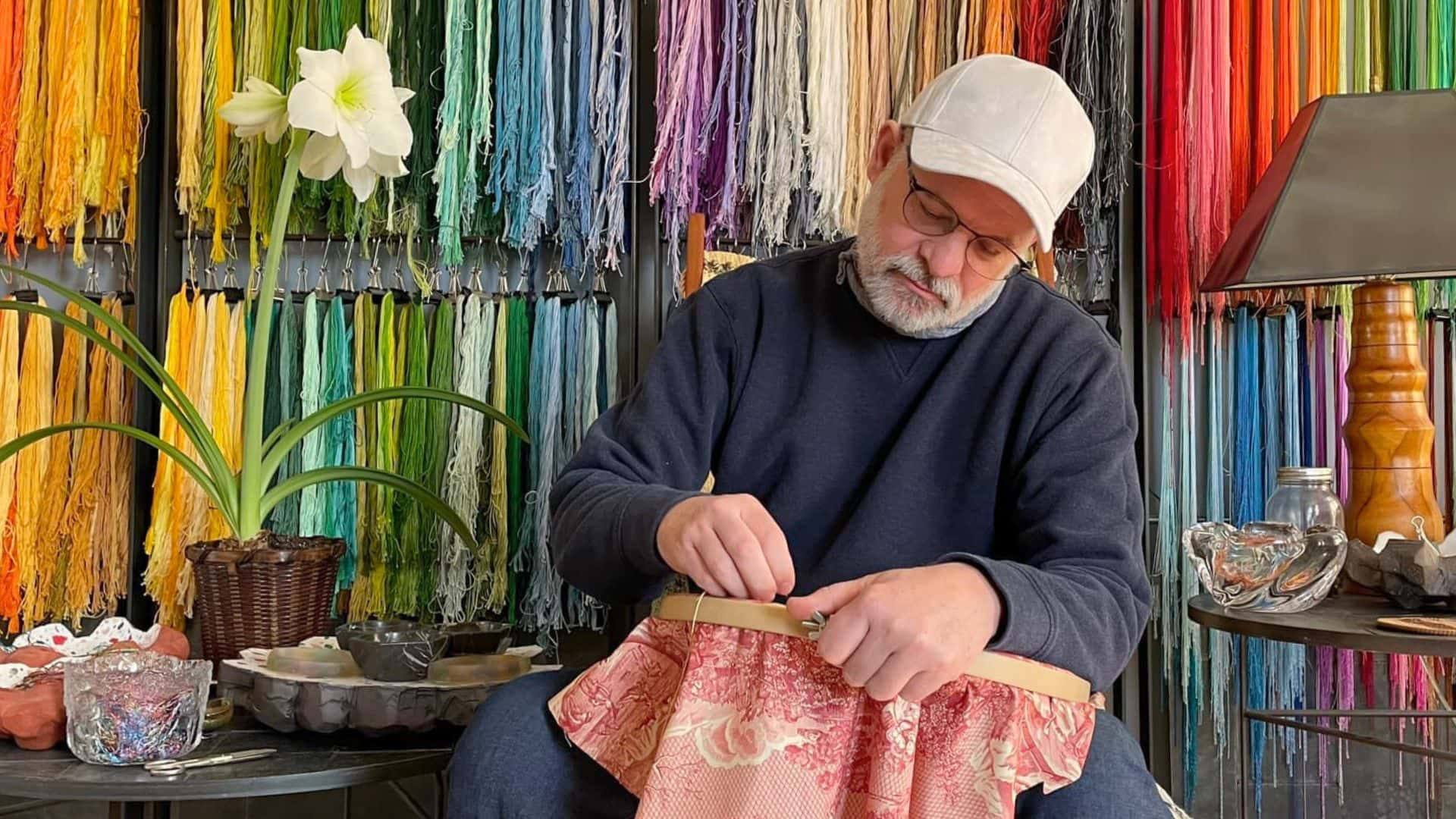 Richard Saja, a textile artist, sits in front of colourful fabric hand stitching one of his artworks.