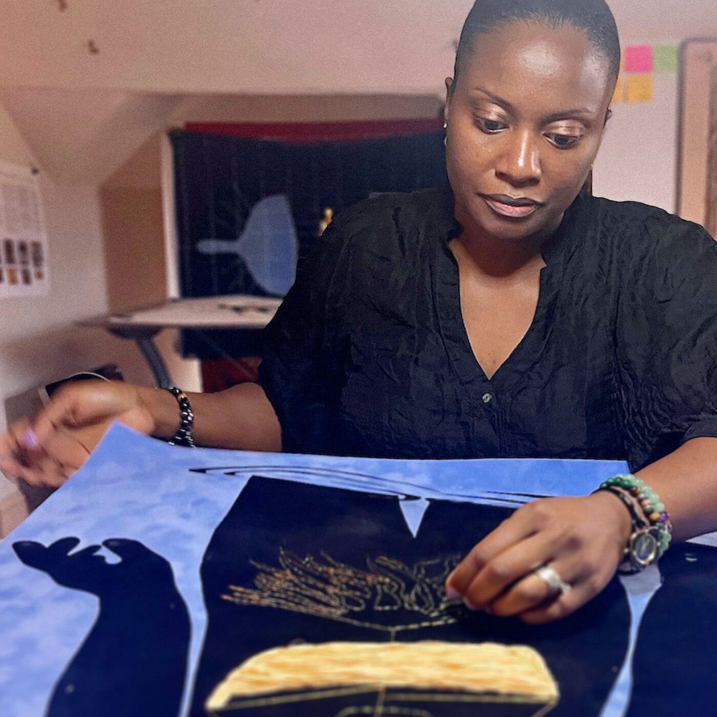 A woman stitching an intricate blue, black and gold artwork in her studio