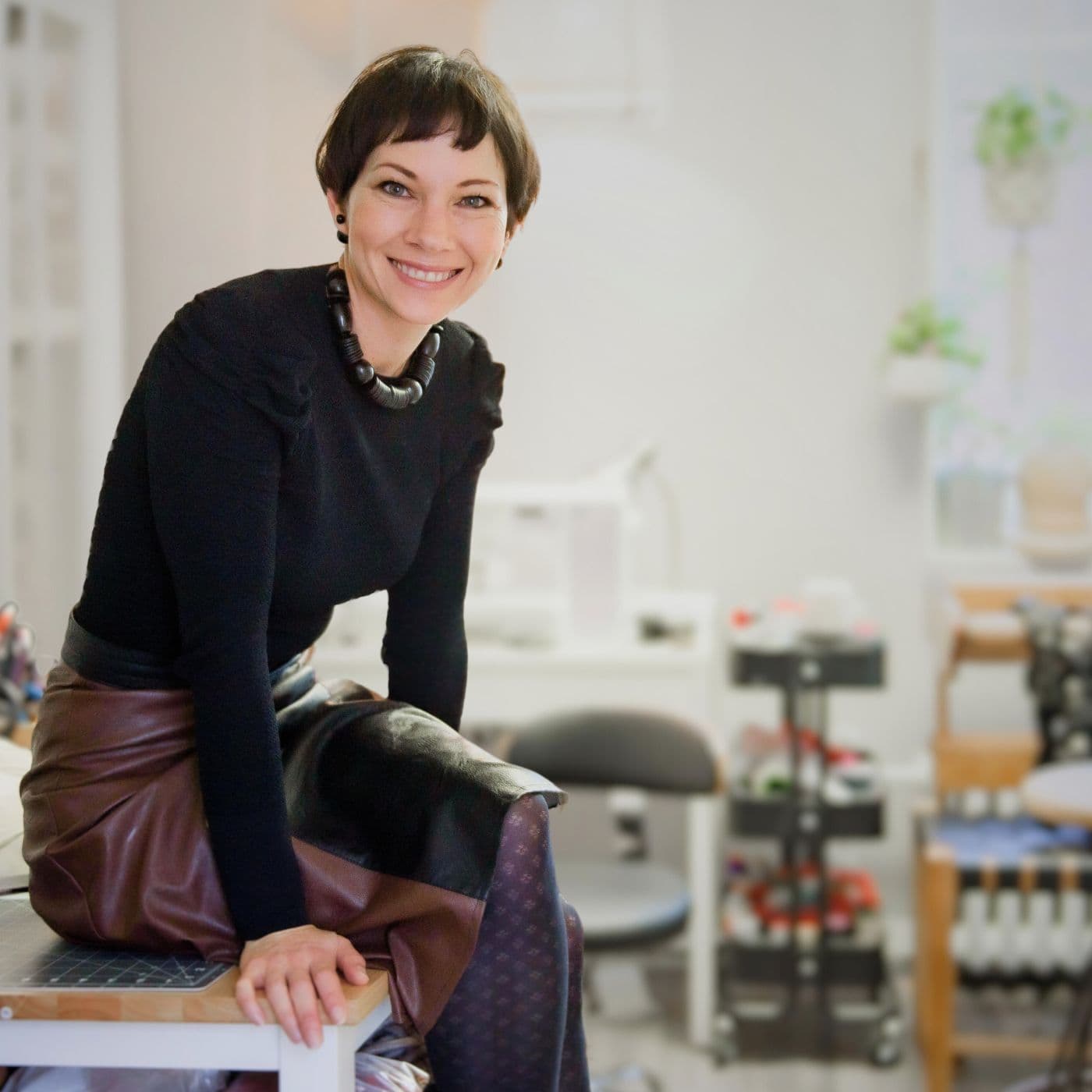 Tina Marais in her studio in Montreal, Quebec. Sitting on a table and smiling at the camera. 