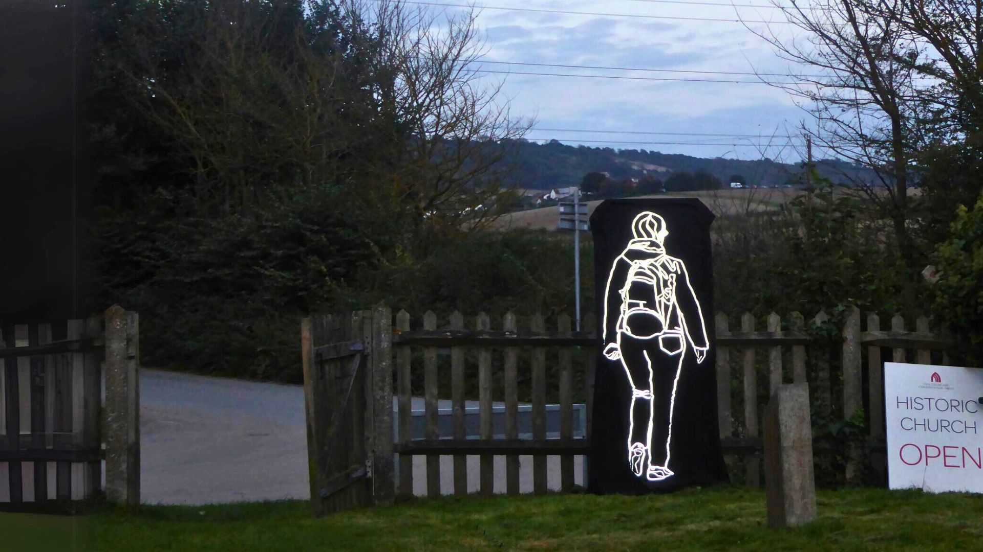 An art installation of a reflective outline of a woman walking in the grounds of a country church