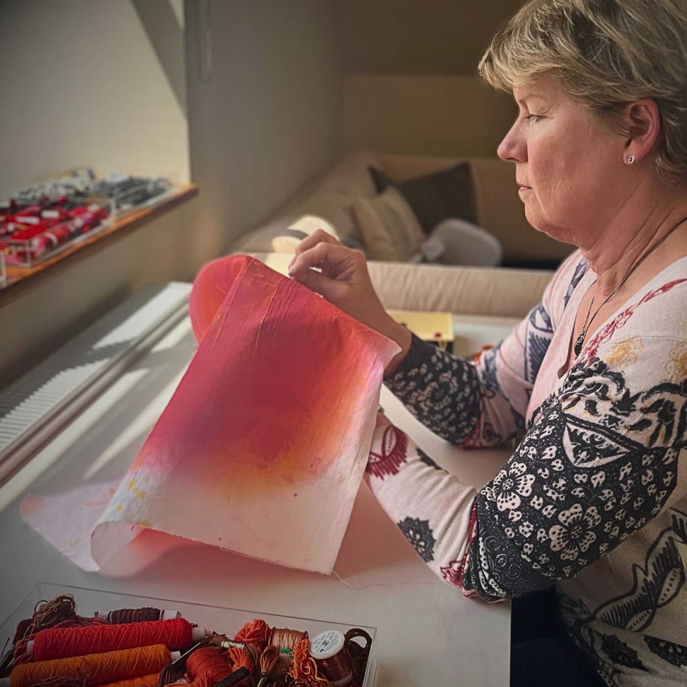 Textile Artist Beverly Ayling-Smith sitting at a table stitching a sample.