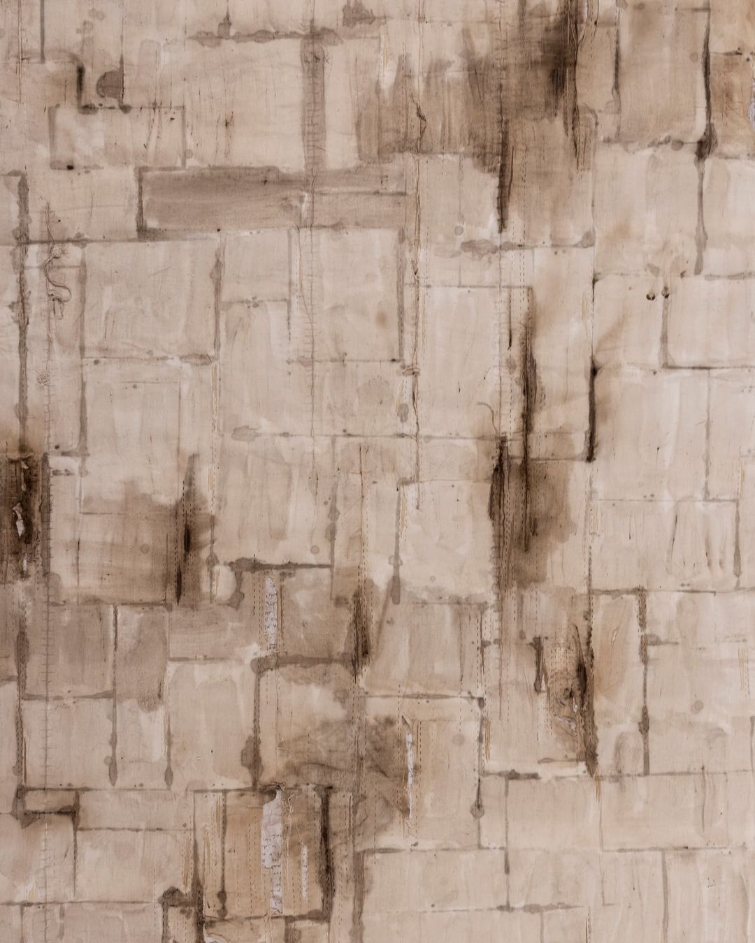 a close up of an artwork of a wall stitched together in a sandstone coloured fabric, with areas of staining and a pattern that gives the impression of bricks. 