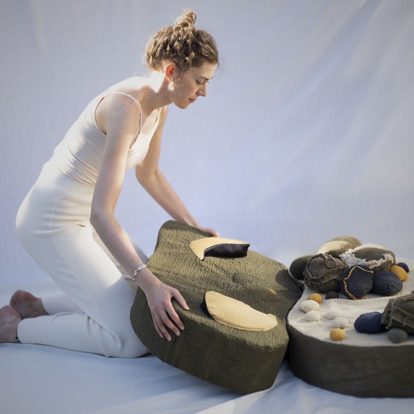 Alice Burnhope kneeling on the floor with her large 'cushion' artwork 'Smudge and Moss'