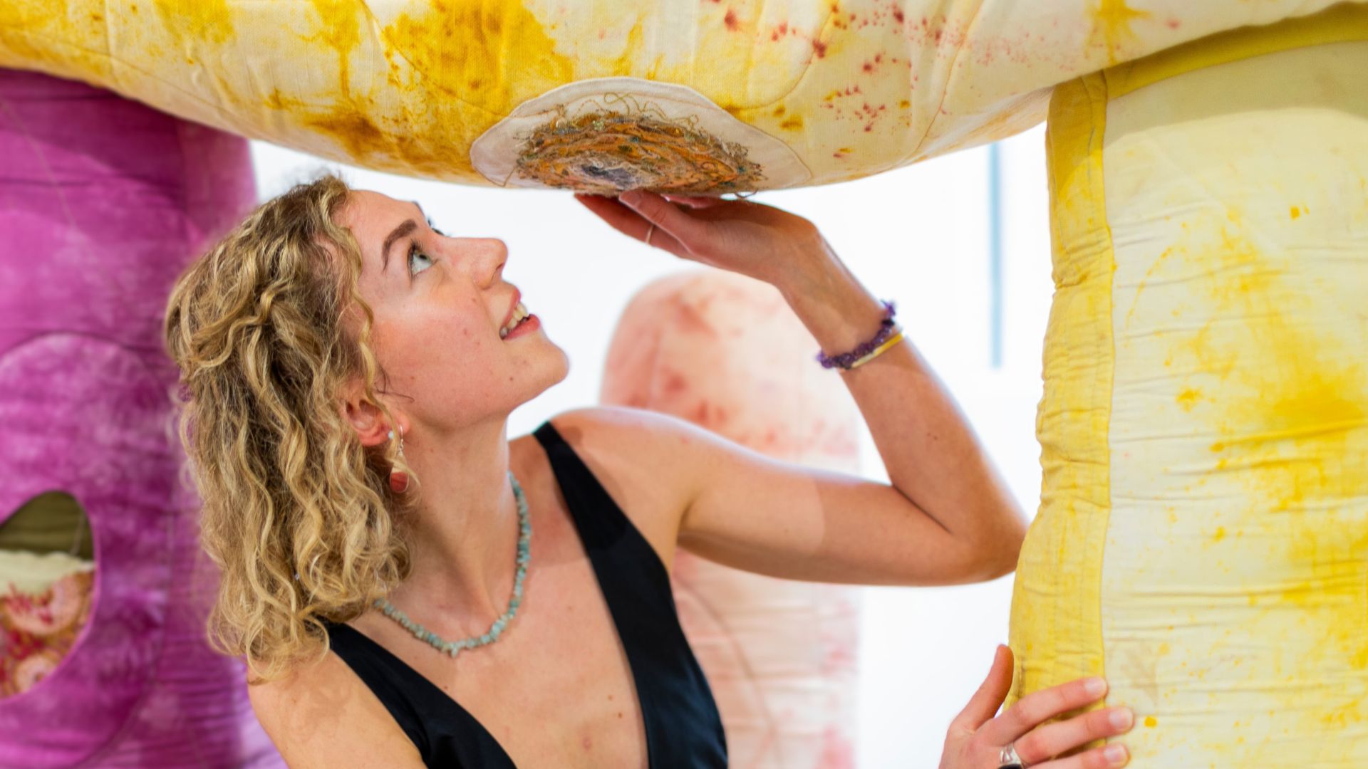 Alice Burnhope stands inside her textile artwork 'Stone Upon Stone' looking up.