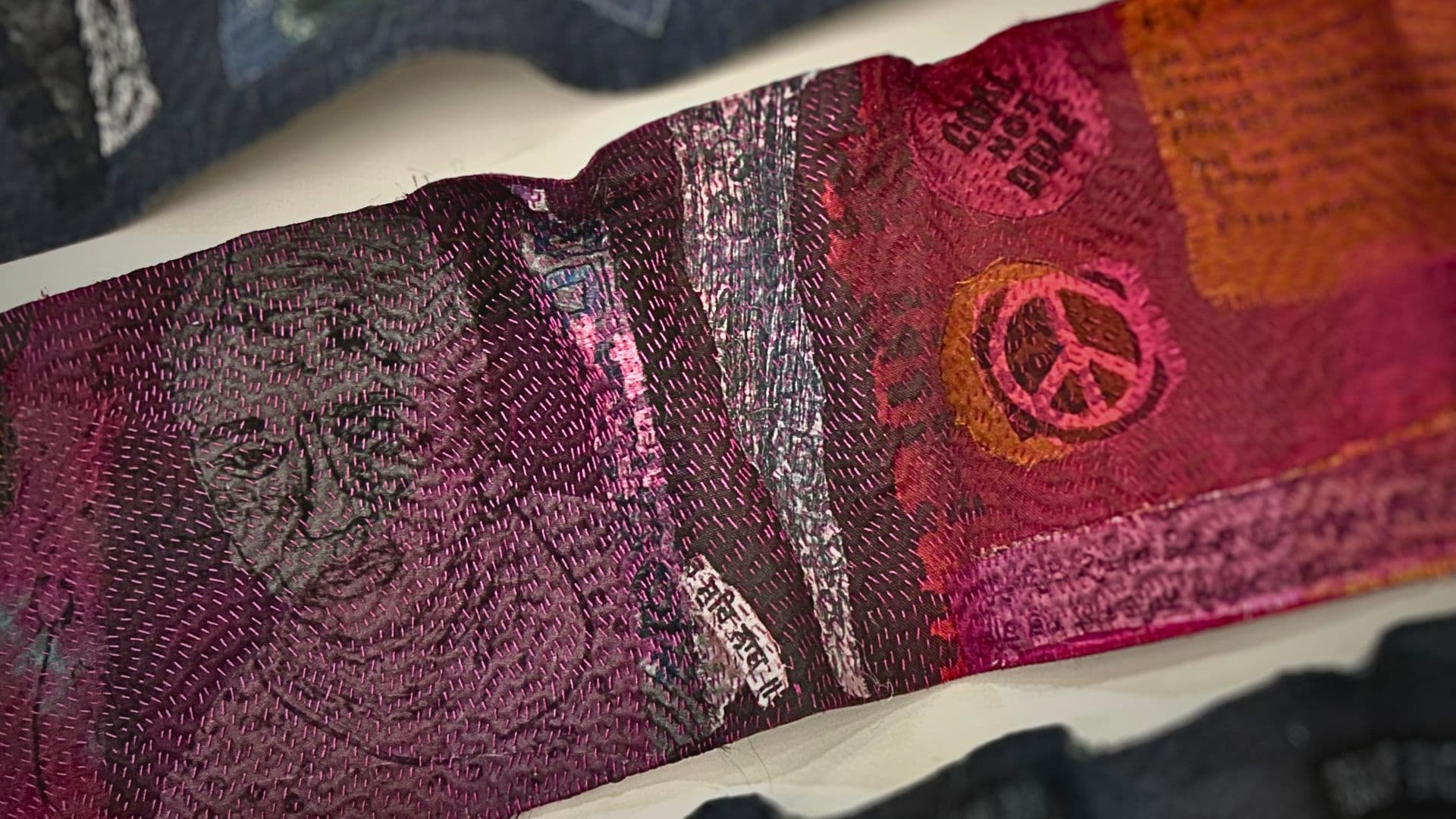 A close up of a stitched artwork embellished with a peace sign and different patterns and stitches. 