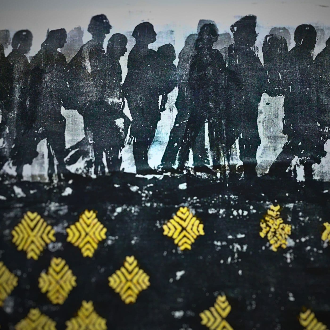 A stitched artwork of a crowd of people in shadow, walking over a black landscape with gold embellishments. 