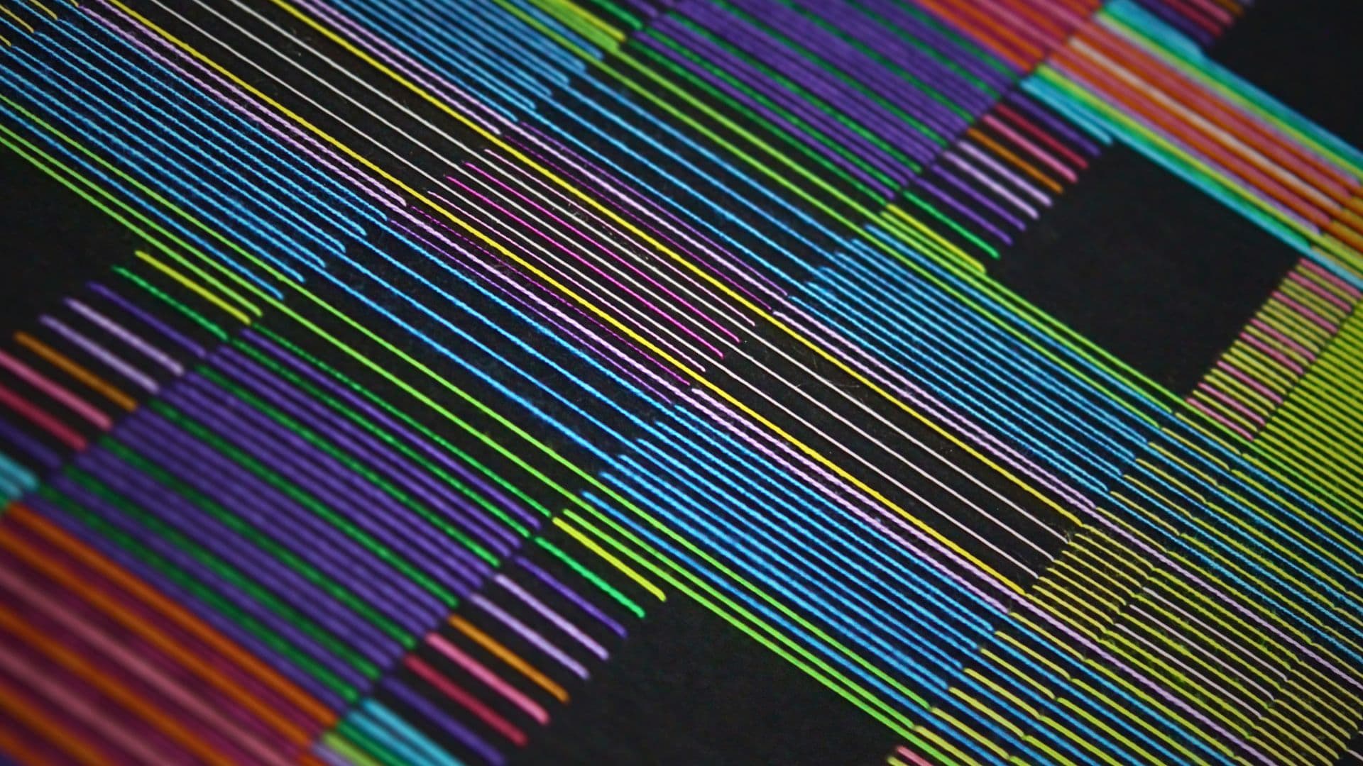 A close up of a colourful stitched artwork in a geometric pattern of stripes.