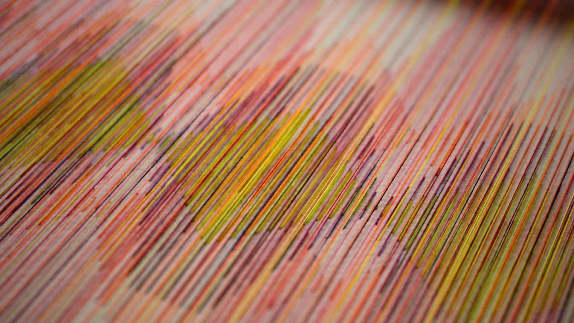 A close up of a colourful, geometric pattern stitched onto a cream background. 