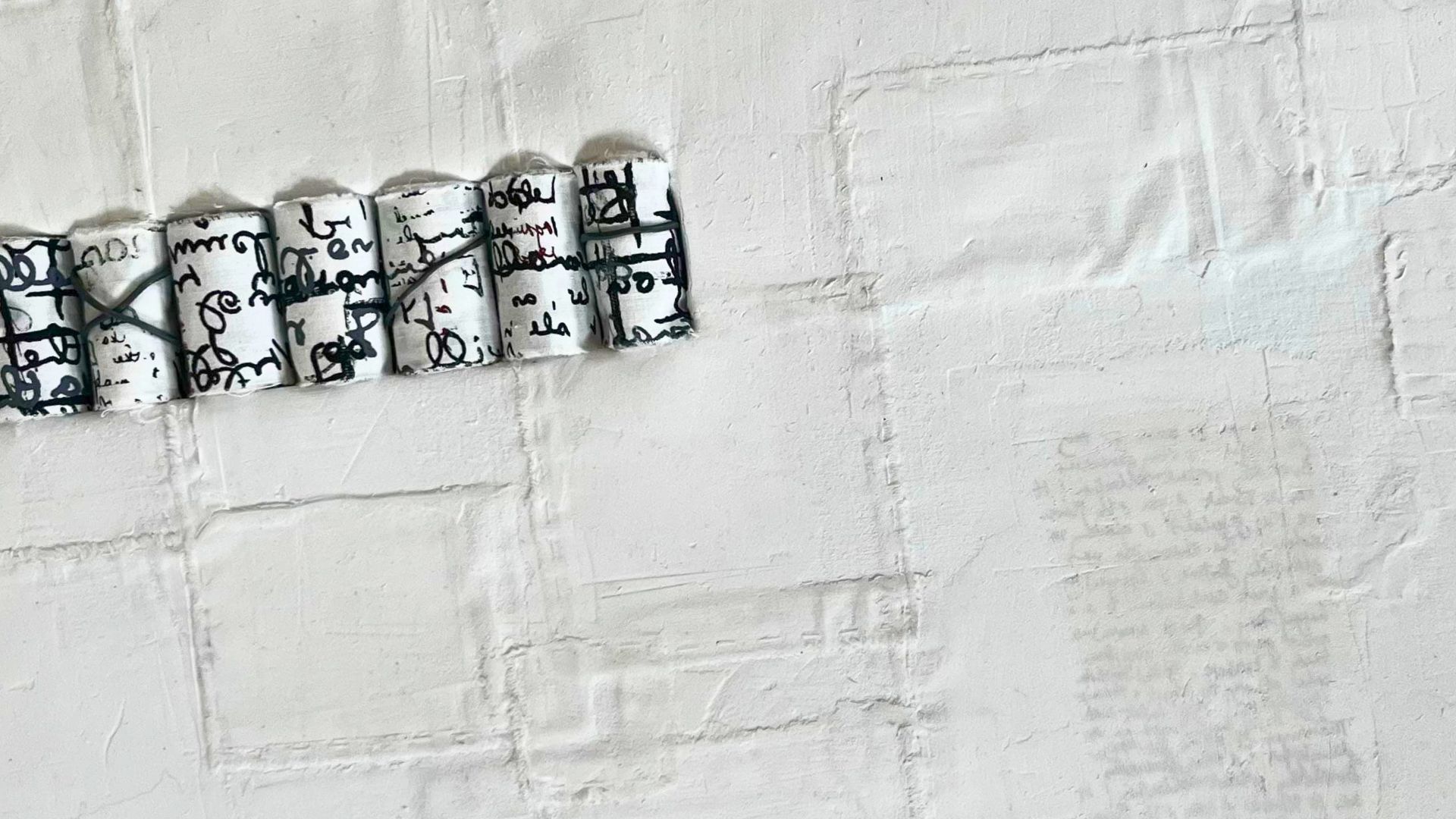 An artwork of rolled up bundles of letters stitched onto a white background.