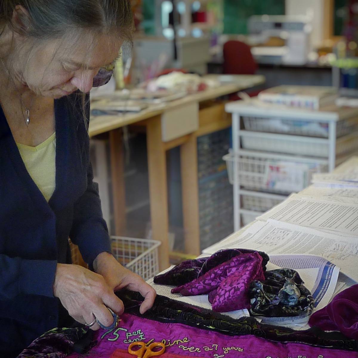 A woman in an art studio sewing a piece of fabric to create an art quilt