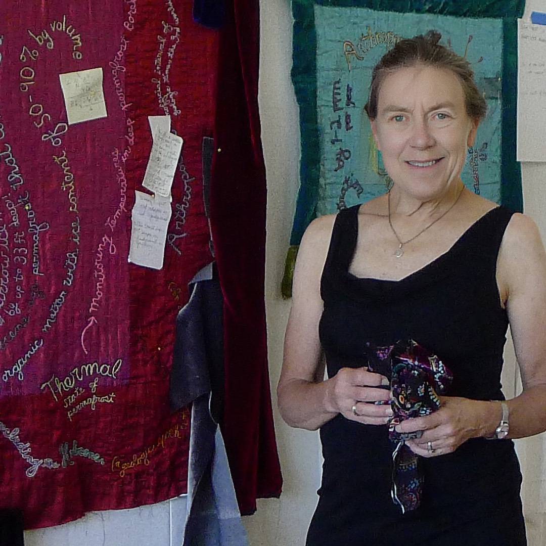 A female artist holding some cloth stood next to textile art in her studio