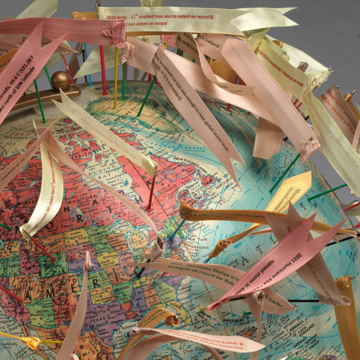 A closeup of a textile art sculpture of a globe with flags pinned over its surface