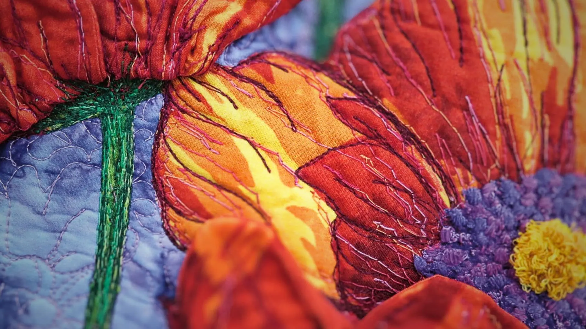 A close-up of an art quilt with a stitched red and yellow flower on a purple background