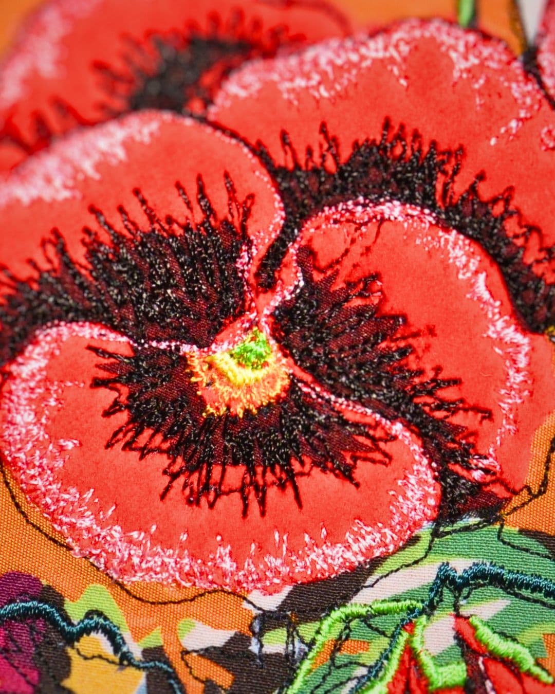 A close up of a stitched artwork of a red flower