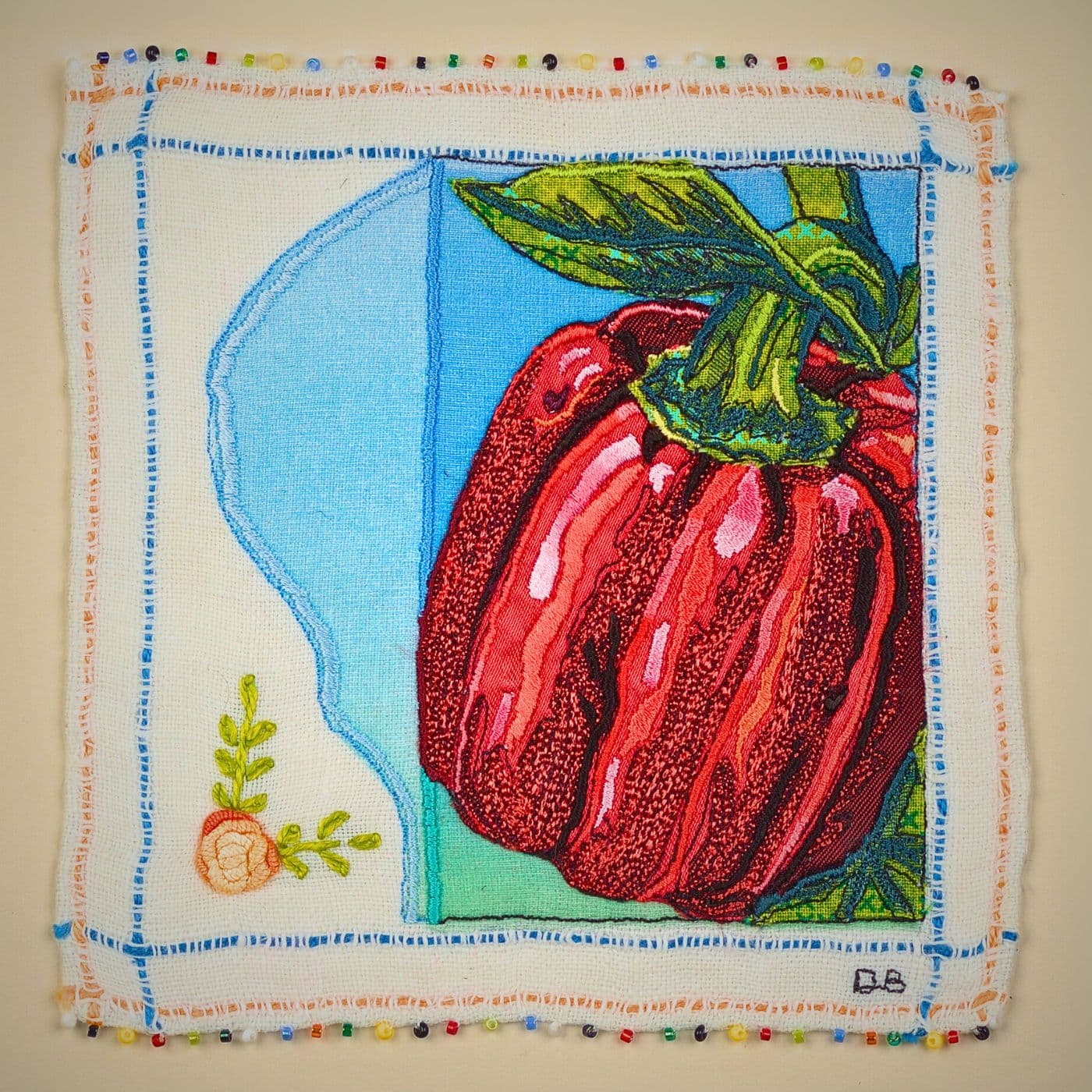 A stitched artwork of a red pepper on a white surface