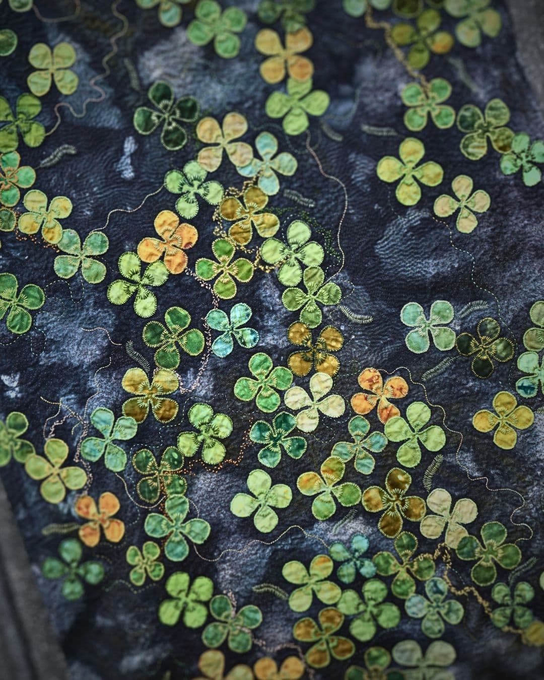 a close up of a fabric stitched with green foliage on a dark background.