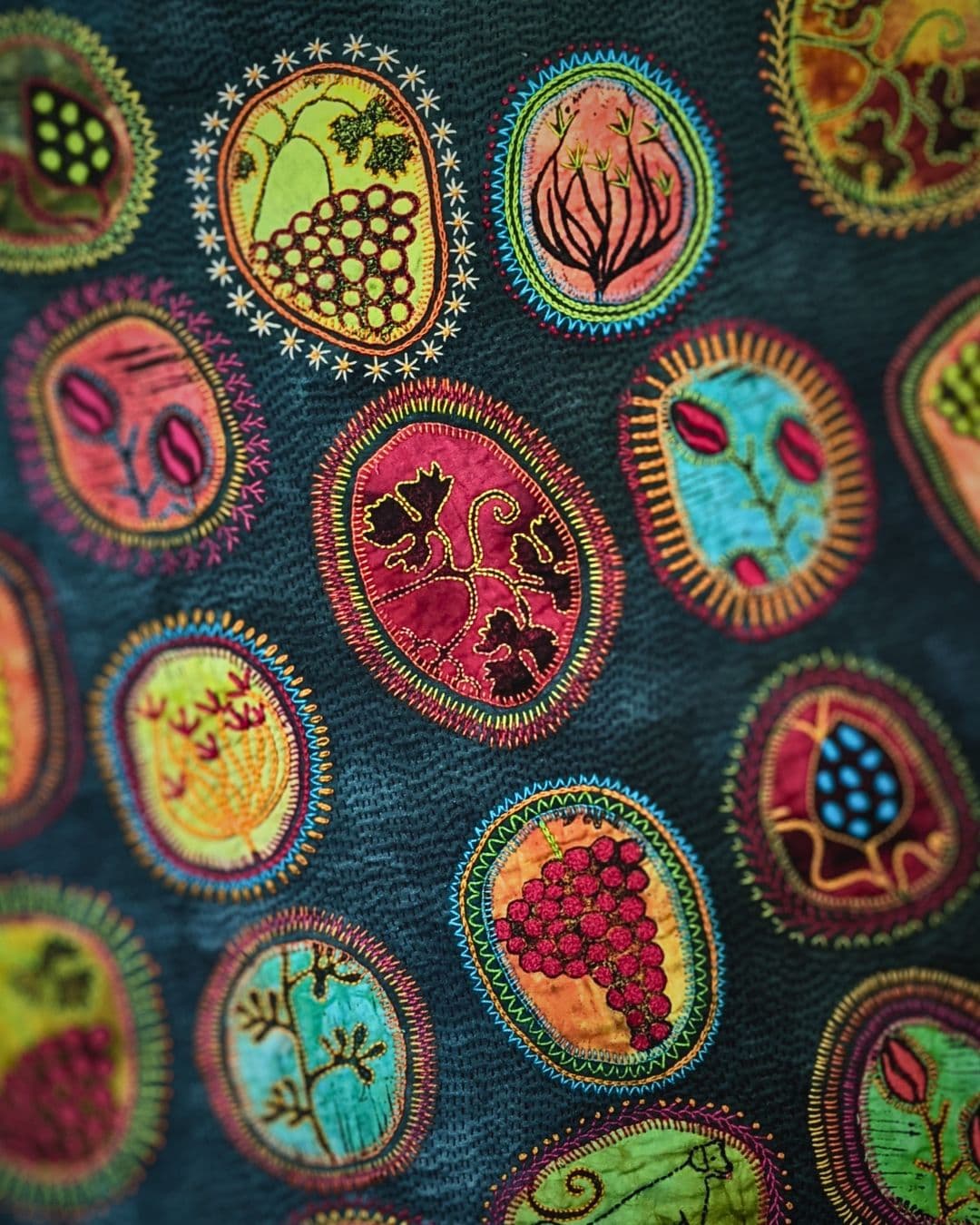 A close up of a stitched artwork with lino-printed motifs in bright colours on a teal background.