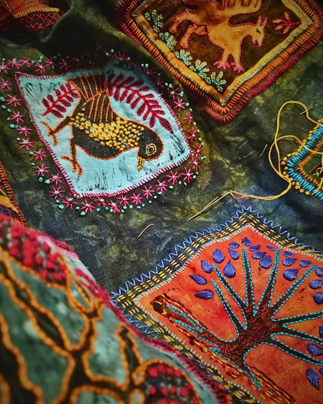 A close up of a fabric artwork embroidered with brightly coloured squares and printed designs.