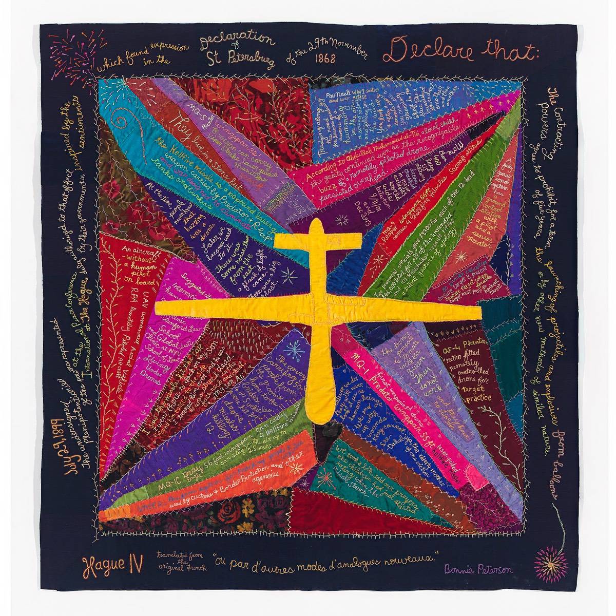 A colorful patchwork art quilt with a bright yellow silhouette of a drone in the center surrounded by thoughts on using drone strikes in war