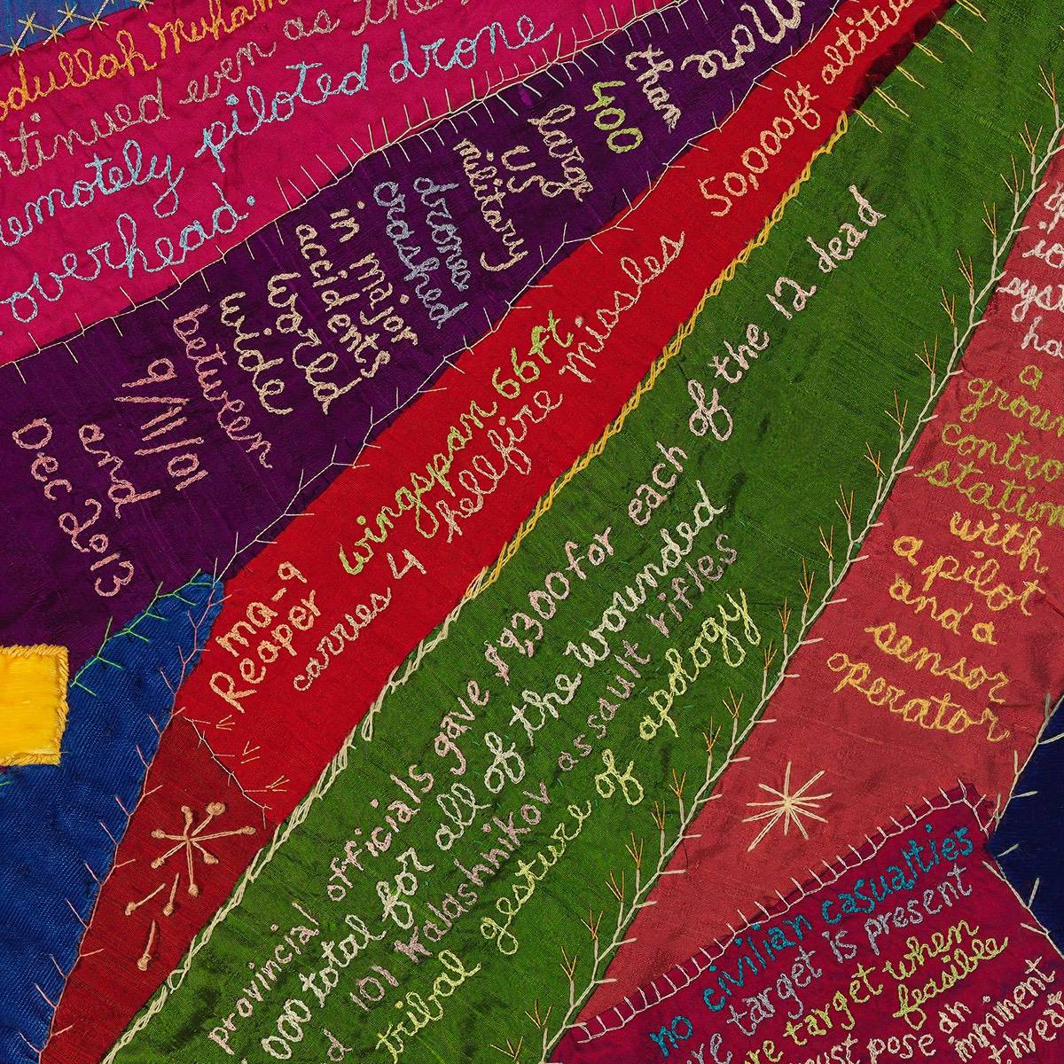 A close-up of a colourful patchworked art quilt with stitched handwriting across it