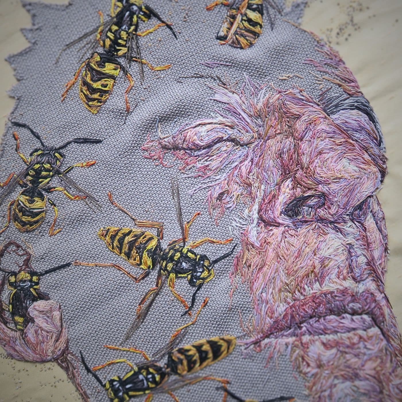 A thread painting of a man's face covered in bees.