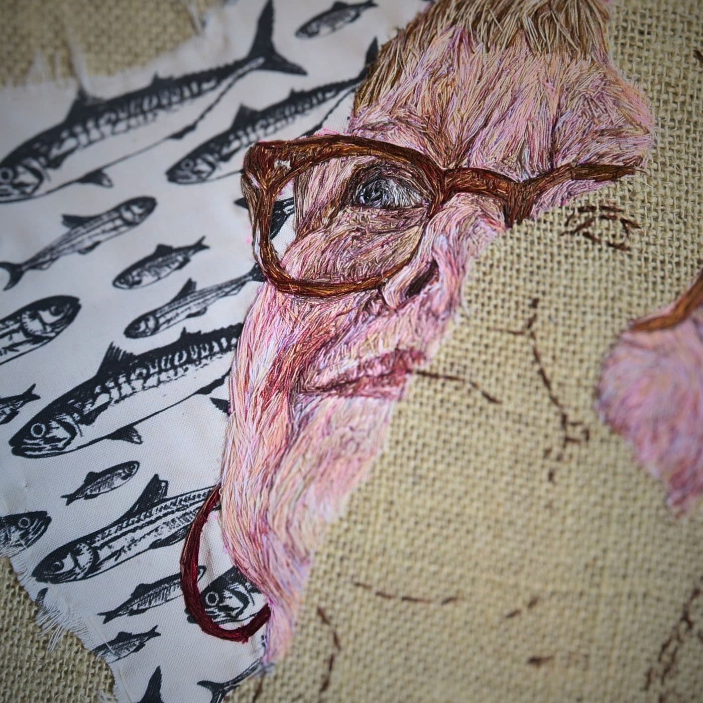 A piece of fabric with a stitched artwork of a woman with a sardine patterned background