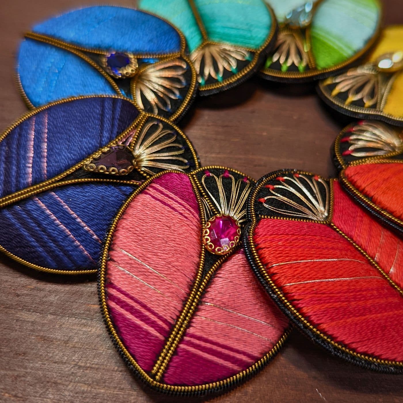 A group of colourful, hand stitched Beetle Brooches arranged in a circle. 