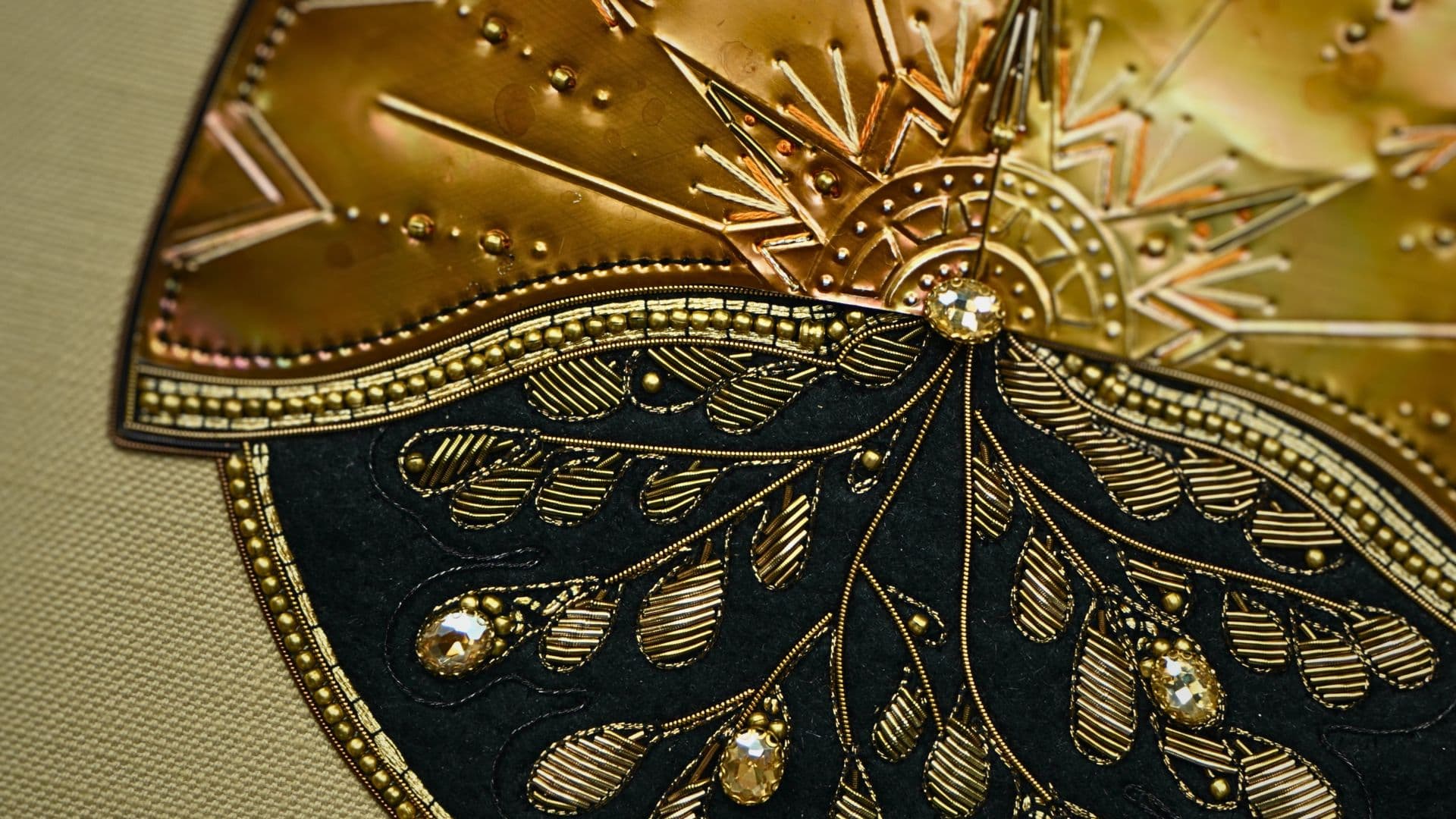 a close up of a gold and black artwork of a breast stitched with beads onto metal. 