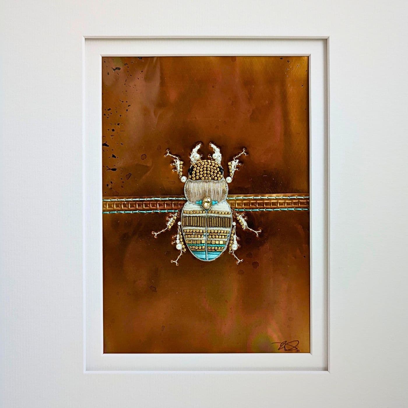 A framed picture of a female stag beetle art work embellished with beads and stitched onto a copper metal background.