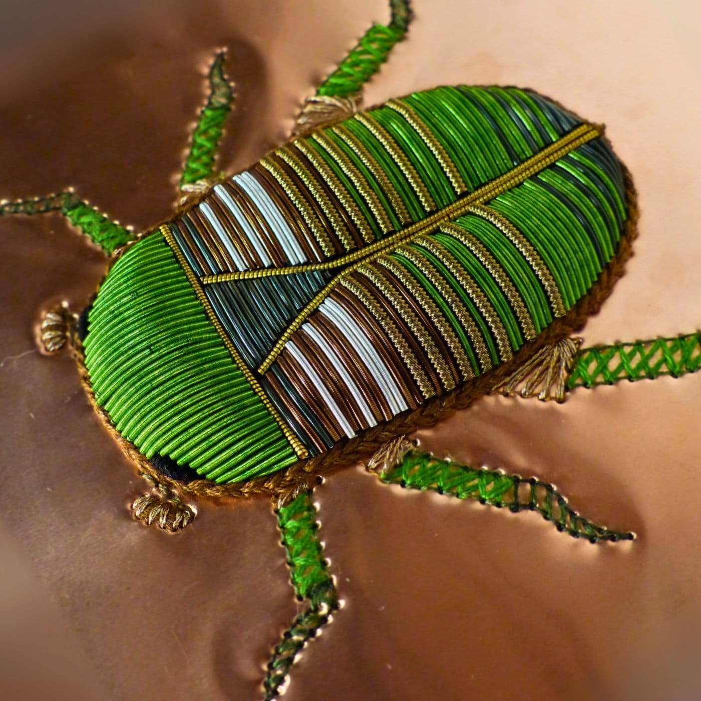 A Close up of a stitched green beetle on a gold surface, embellished with beads. 