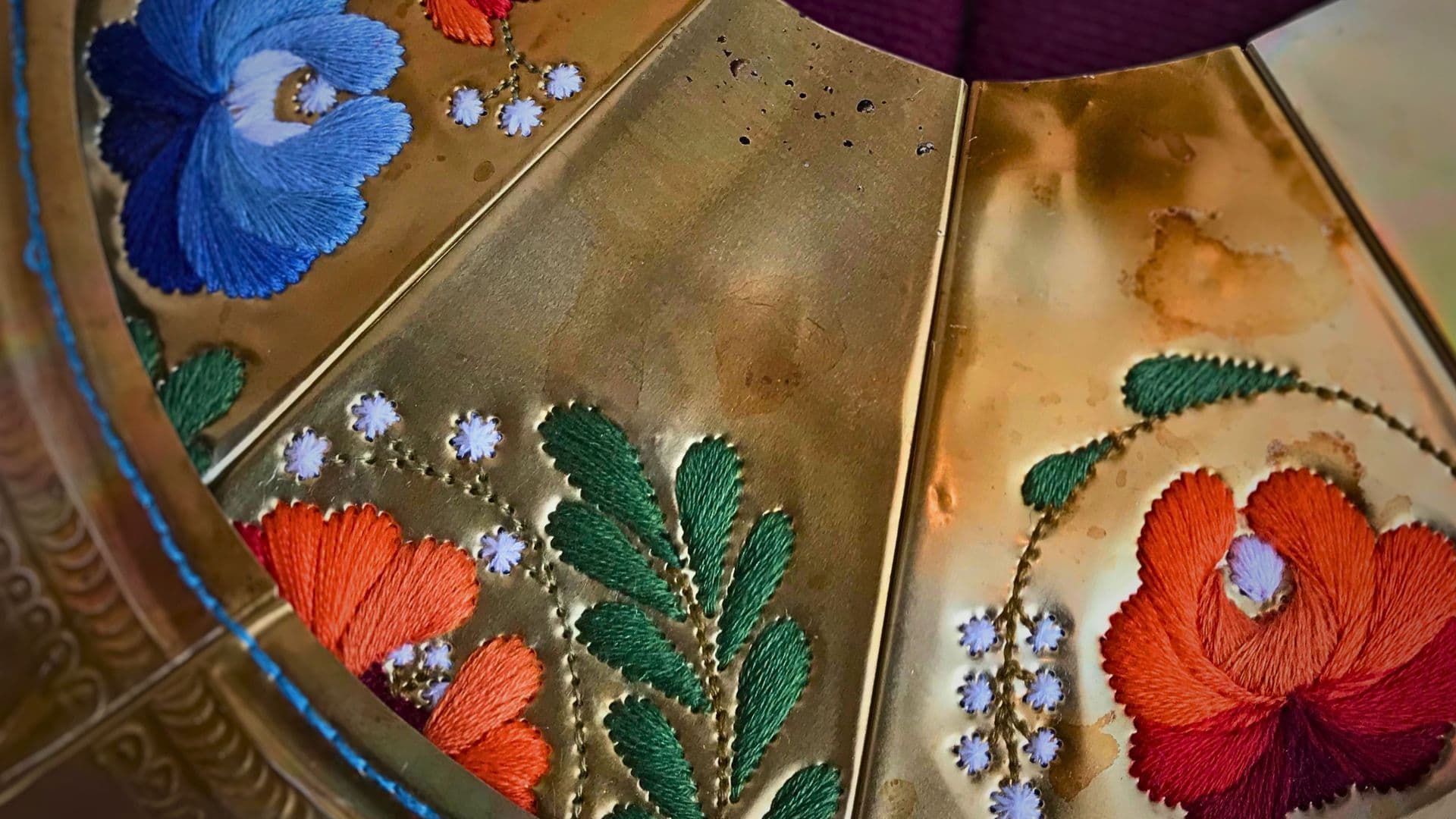 A golden metal plate with colourful embroidered flowers.