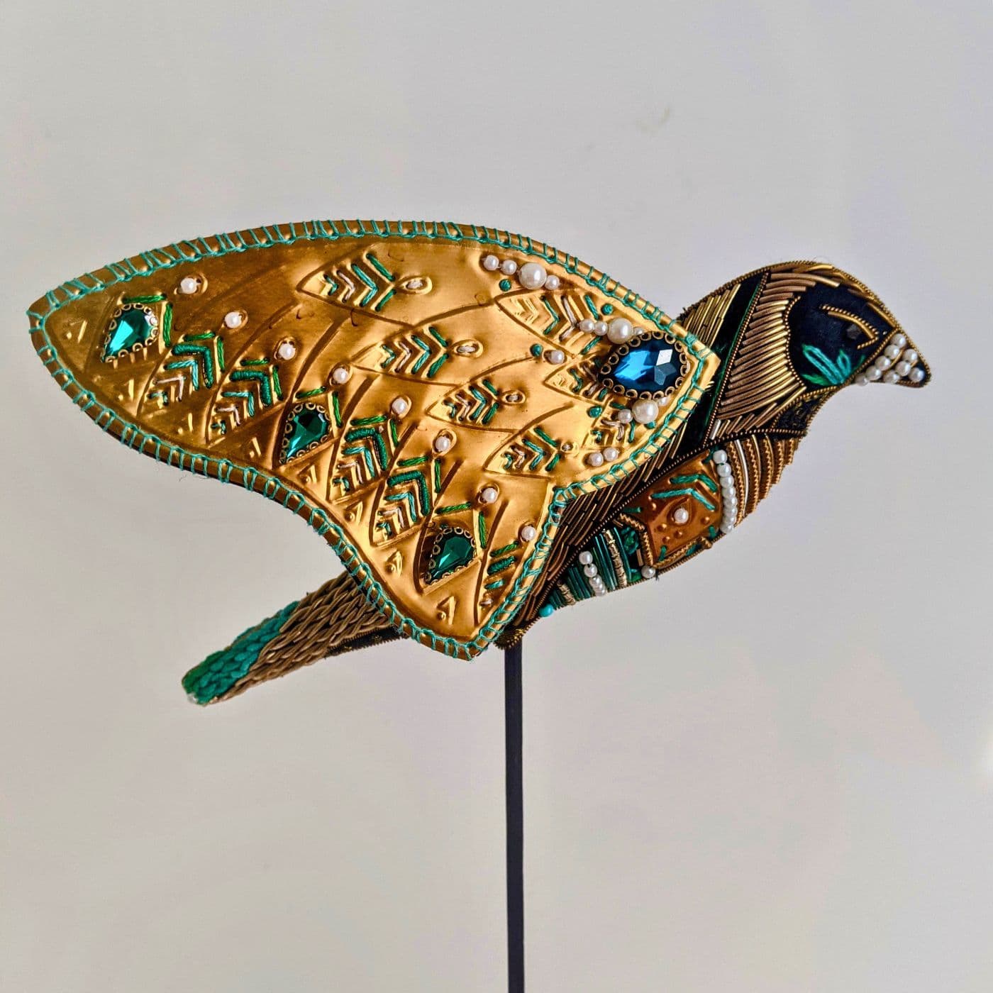 An art work of a gold bird  on a stick, embellished with blue and green gems.