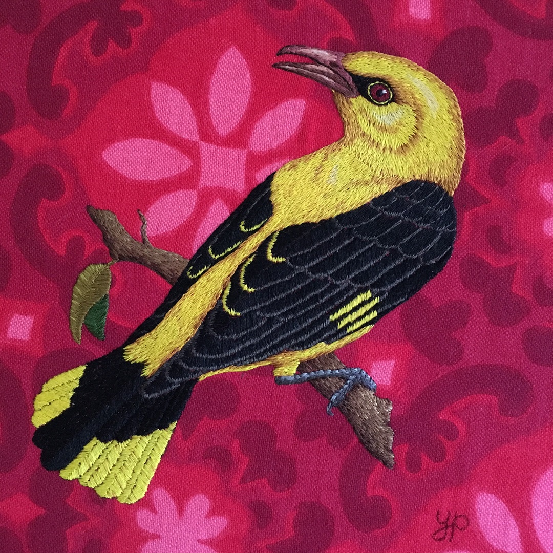 An embroidery of yellow bird on a pink patterned fabric. 