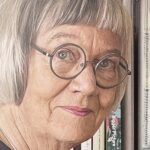 Portrait of Gwen Hedley, a textile artist, wearing glasses and surrounded by books, reflecting her wisdom and experience