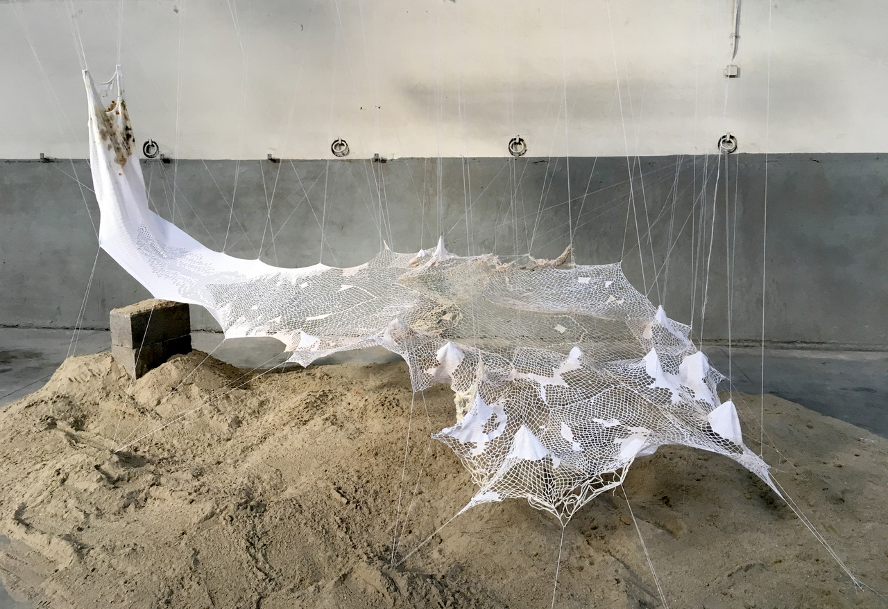 TRANSVERSUS /Performance  2020. Work in progress since 2017 Size of piece- variable dimensions : 400 x 500 x 250 cm Material and techniques : Cotton thread, wood, sand, oars, concrete, handmade lace, oil painting, hand stitching.  Installation work by Sónia Aniceto Performance by Maria João Flôxo  Poème : Aline Yasmin Sound interventions: Alex Cepile, voice Fanny Photos: Erwin Boosten, Monica Musoni