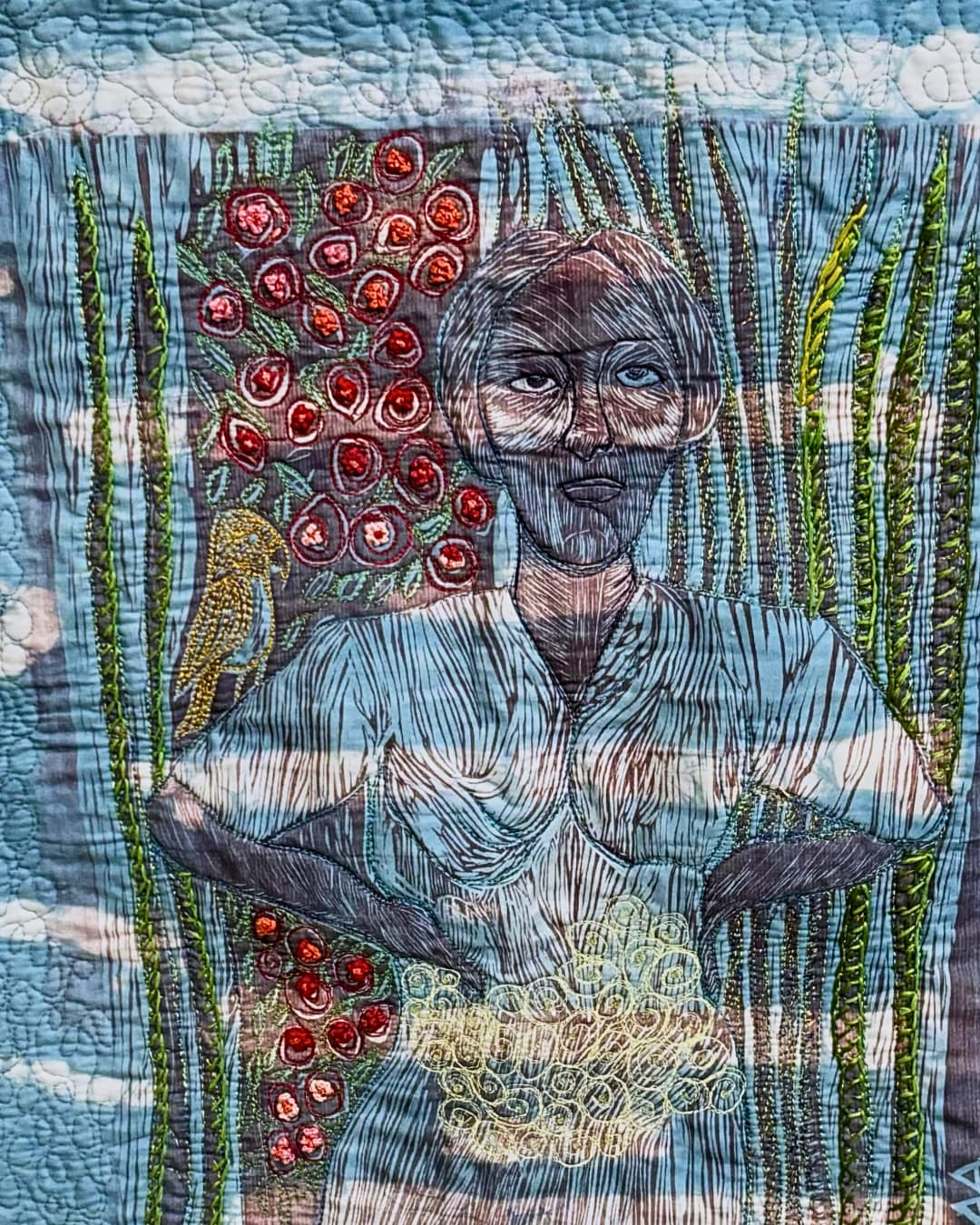 A close up of a quilted artwork of a woman stitched onto a blue background.