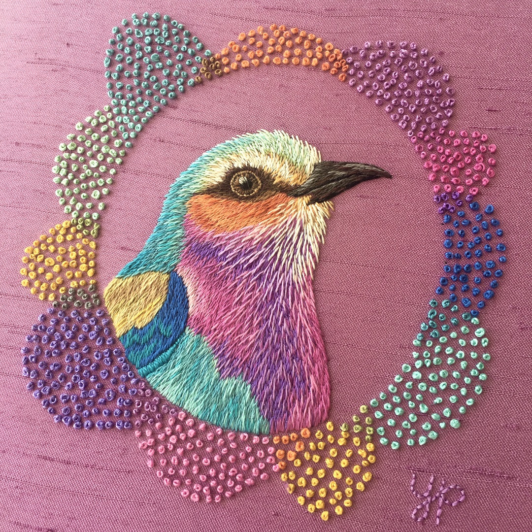 A colourful bird embroidery on a pink surface fabric background.