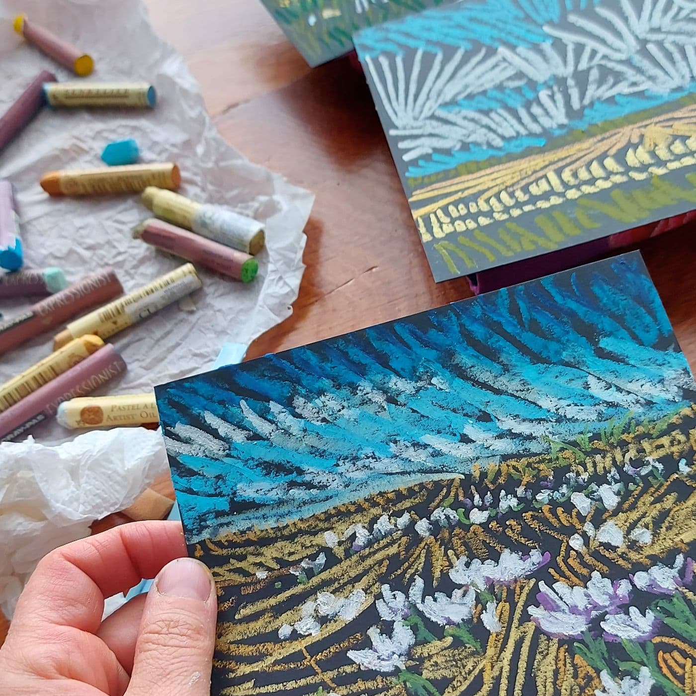 A hand holding an oil pastel sketch in preparation for yarn stitching.