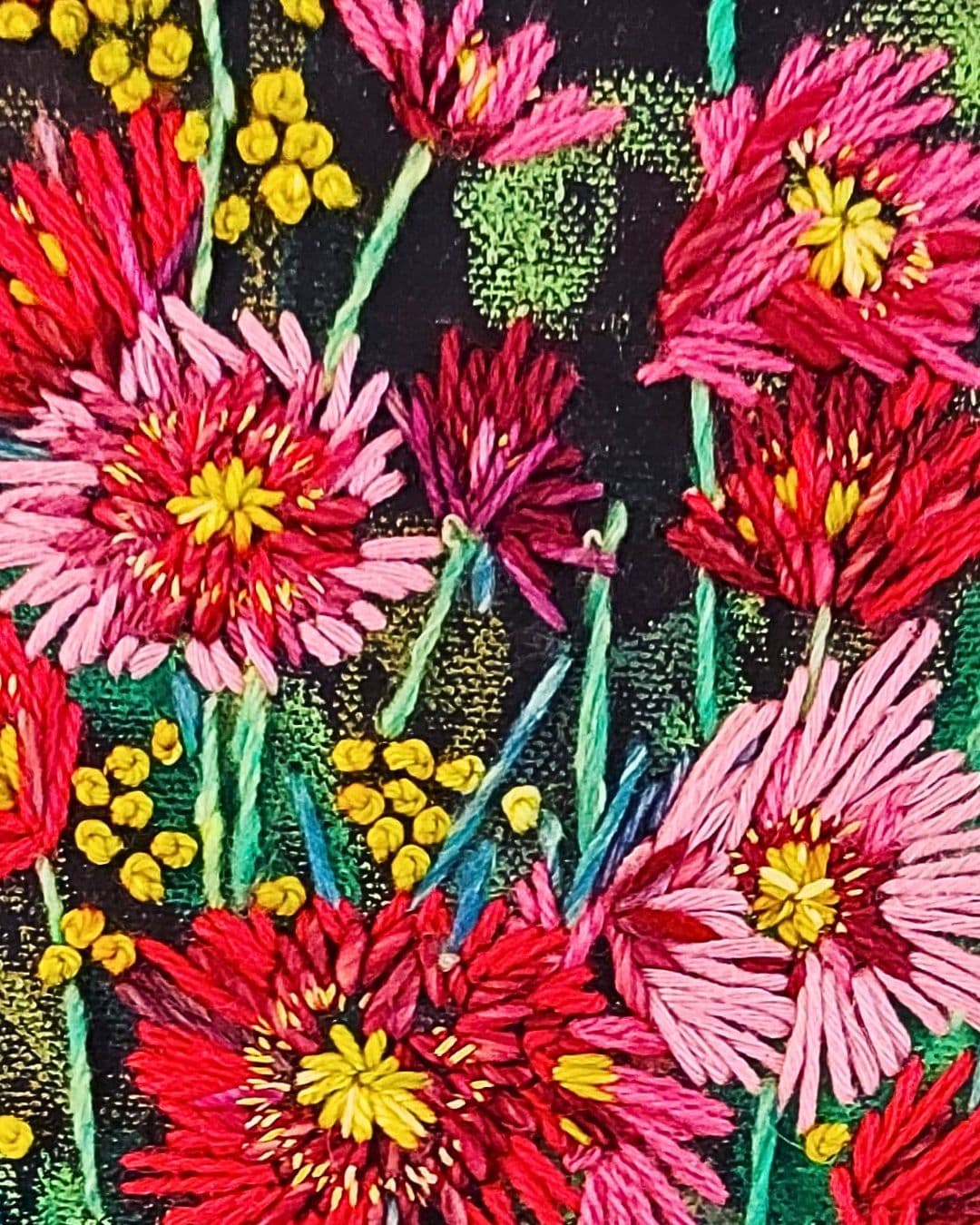 A close-up image of a hand stitched bunch of red and pink flowers on a black background