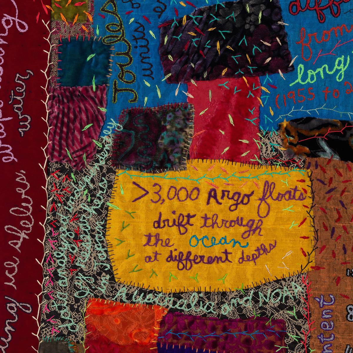 A close up of a colourful patchwork art quilt with stitched writing across its surface