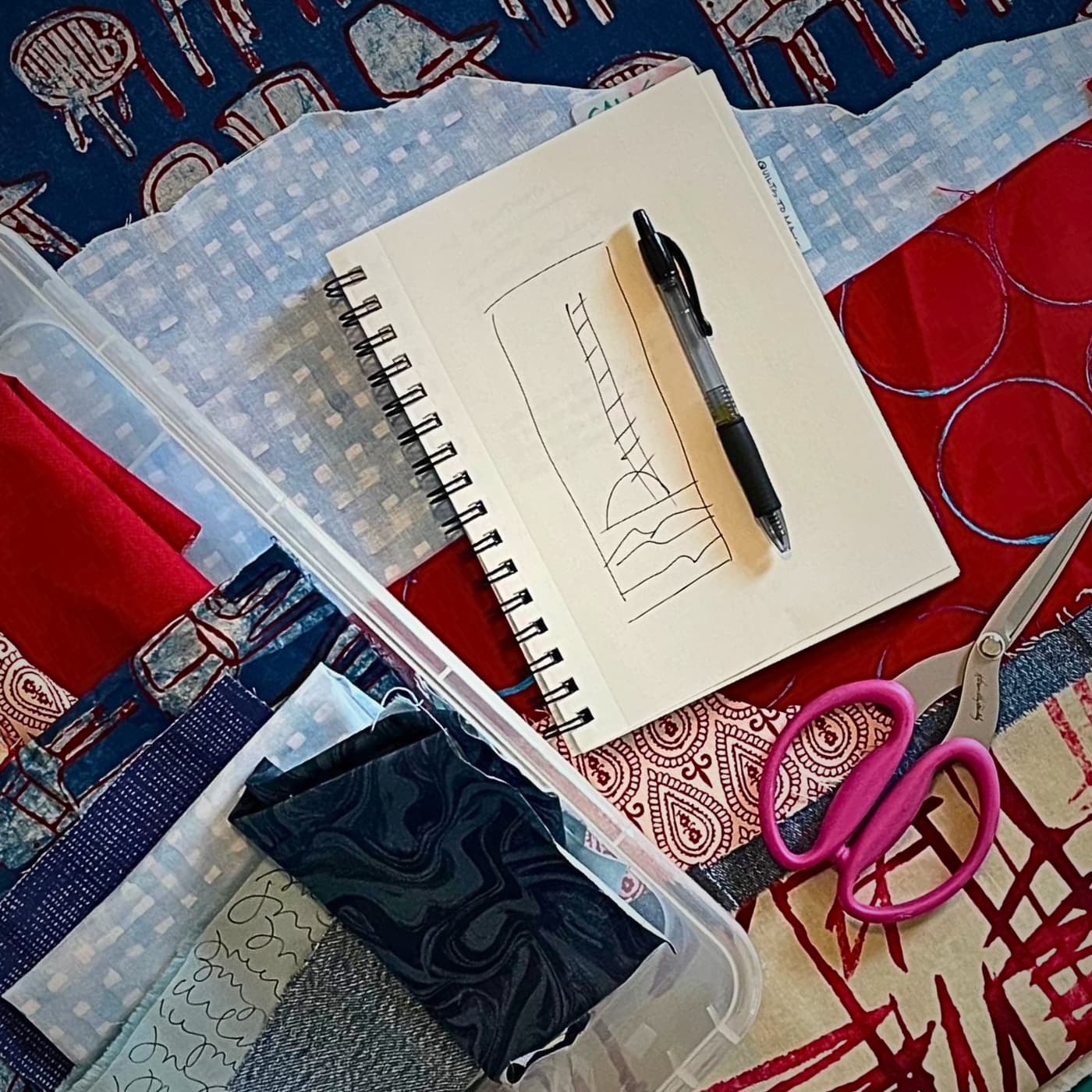 A notebook with a pen and scissors on a quilt