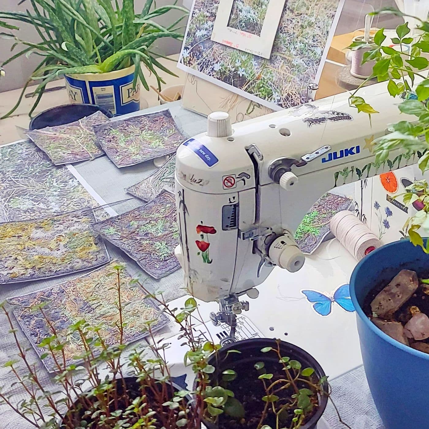 A sewing machine surrounded by plants on an artist work table