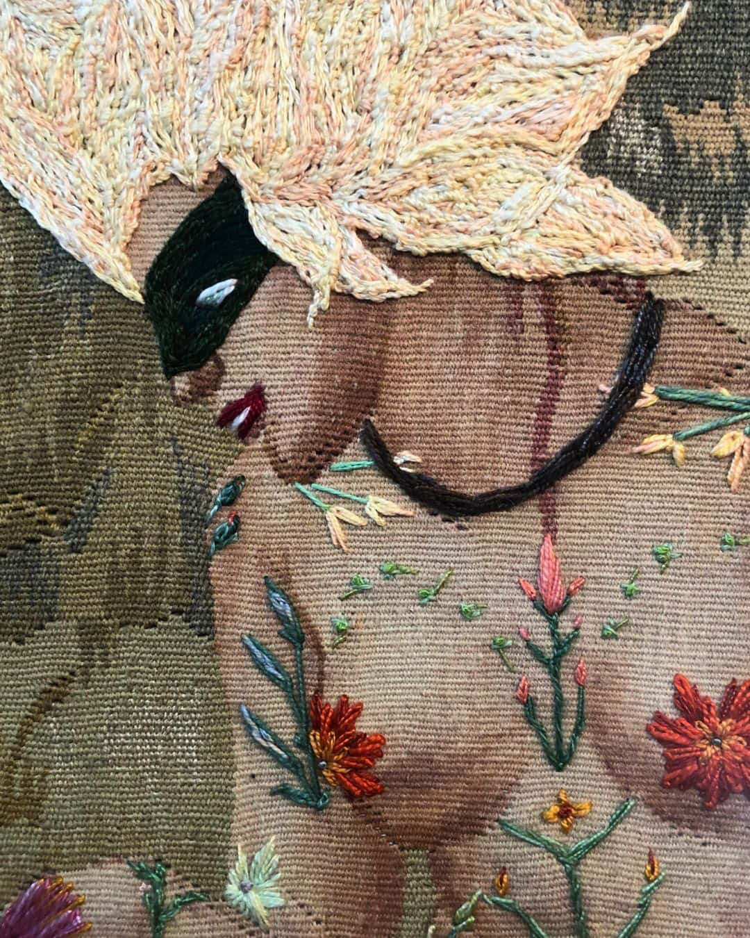 a close up of a tapestry of a woman looking down. She is nude, except for a domino mask and flowers which decoratively cover her body.