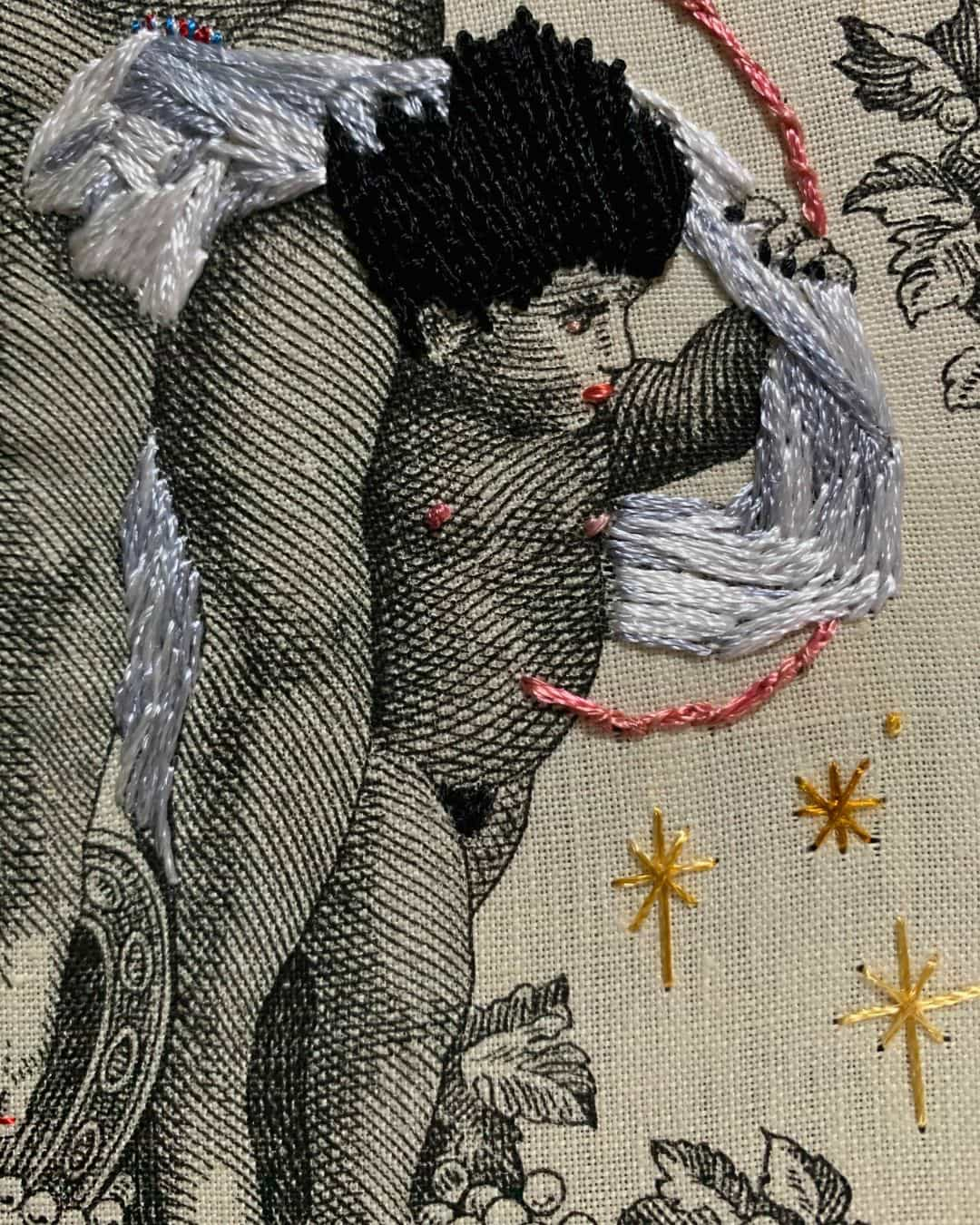 a close up of a fabric image of a cherub with hand-stitched black hair and a pink umbilical cord connecting to his mother above his head and out of sight.